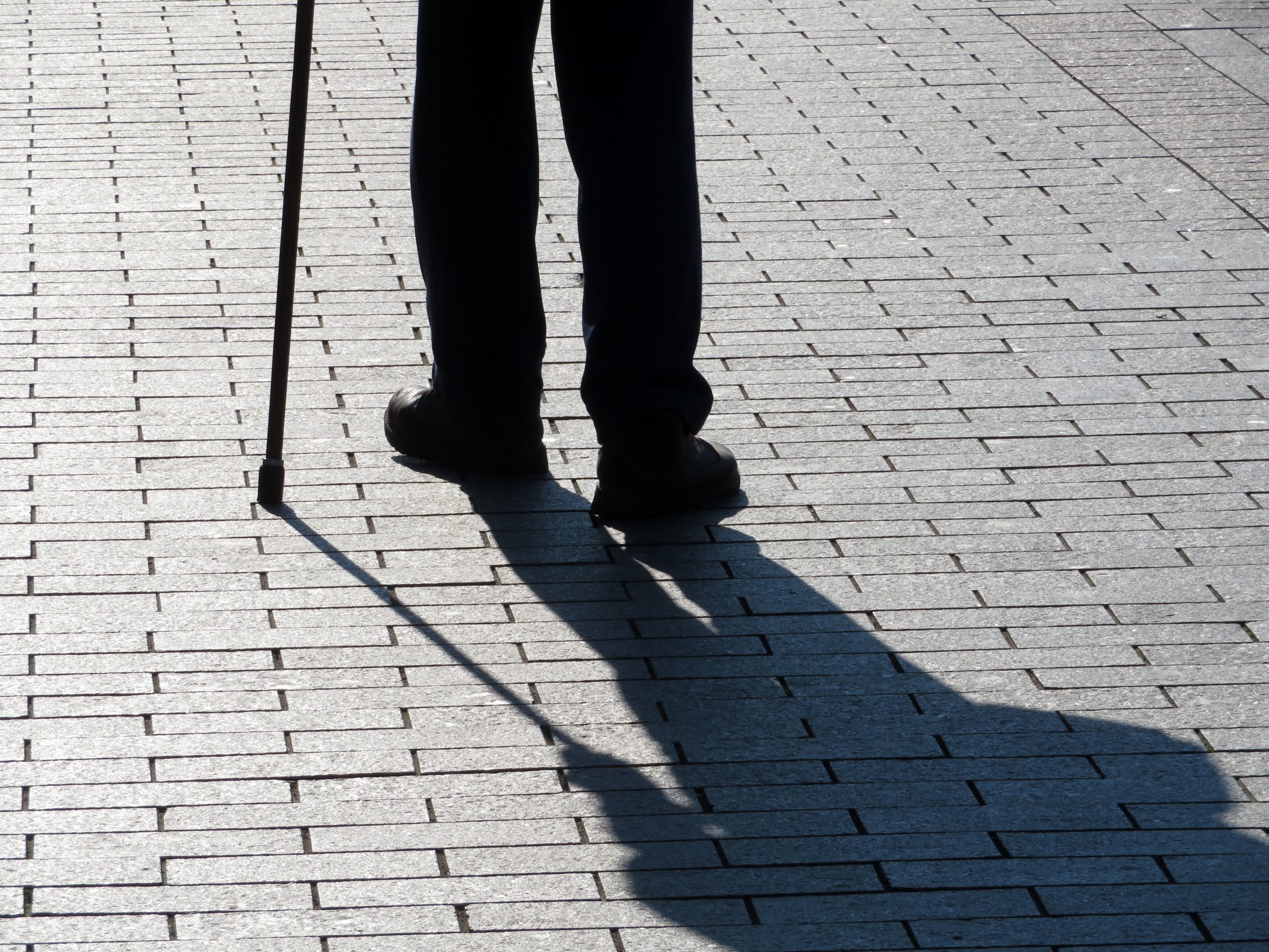 Silhouette of man walking with a cane, long shadow on pavement