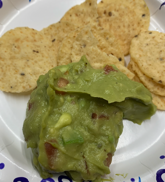 To show the guacamole dip after it has been made and plated alongside tortilla chips.
