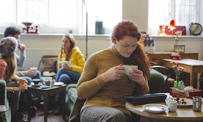 Transgender woman sitting contently with a coffee and looking at her digital tablet