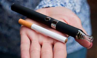 closeup of hand holding a vape pen and a traditional cigarette