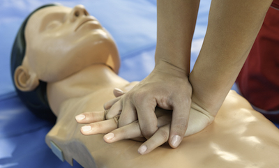 Hands performing chest compressions on CPR dummy