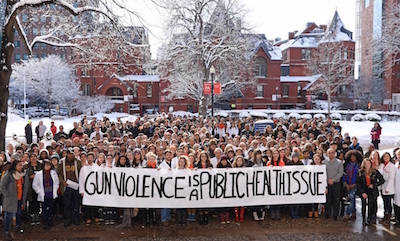 BU Medical Campus walk-out for gun violence; crowd stands in front of SPH's Talbot Building in the snow, holding a banner that reads "Gun VIolence Is a Public Health Issue"