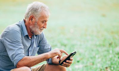 Senior man using a smartphone while sitting on grass in the park