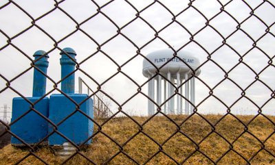 Water tower of Flint Michigan through a chain linked fence.