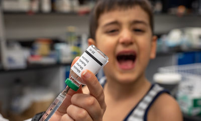 Close-up of preparing a measles mumps and rubella vaccine, with child crying in background at the sight of the needle