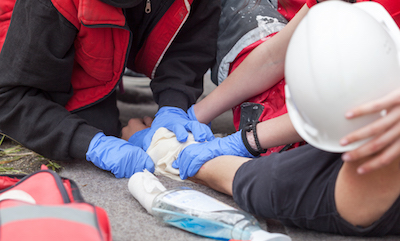 Two people provide first aid to an injured worker wearing a hard hat