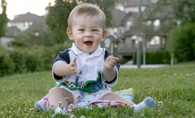 Clapping 9-month old sitting up on a lawn.