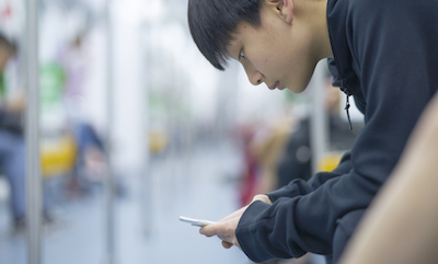 Asian teenage boy using smart phone on public transit