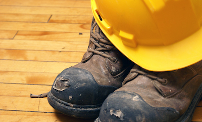 Helmet and dirty steel-toed boots on the floor in a home.