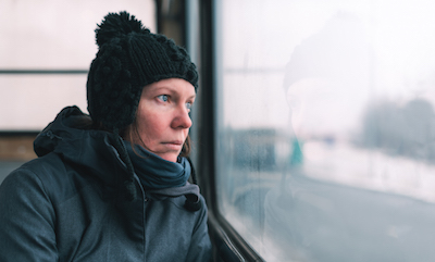 A woman looks out a bus window at a winter landscape.