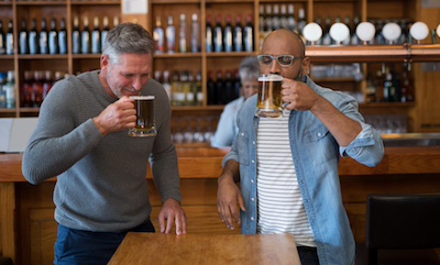 Two middle-aged men drinking beers at a bar