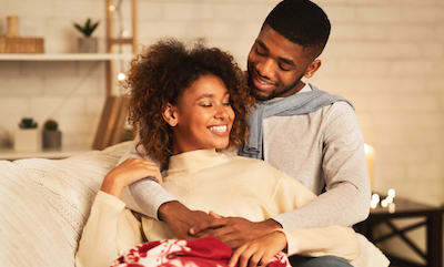 Couple in sweaters cuddling on couch under a blanket