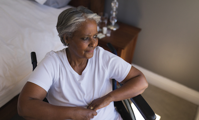 Senior African American woman in wheelchair looking worried through window at home