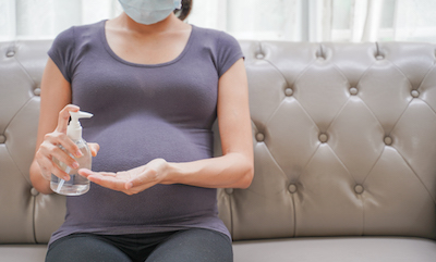 Pregnant woman wearing a mask and using hand sanitizer