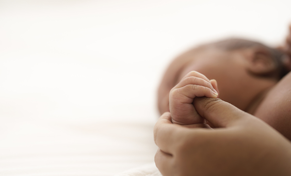 african american infant baby lying on bed while mother hands pull baby up