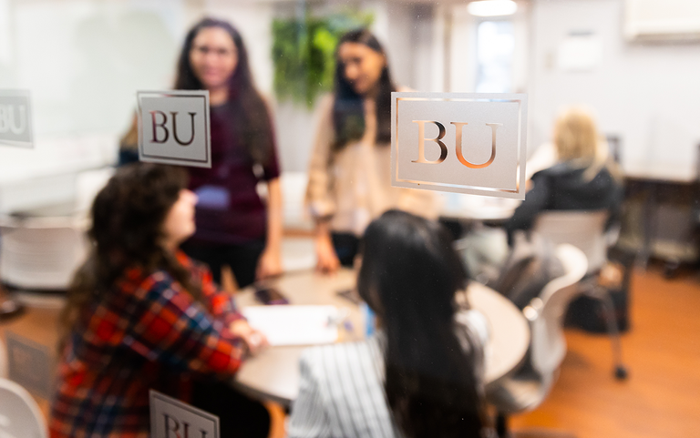 Students gather around a table, blurry behind glass