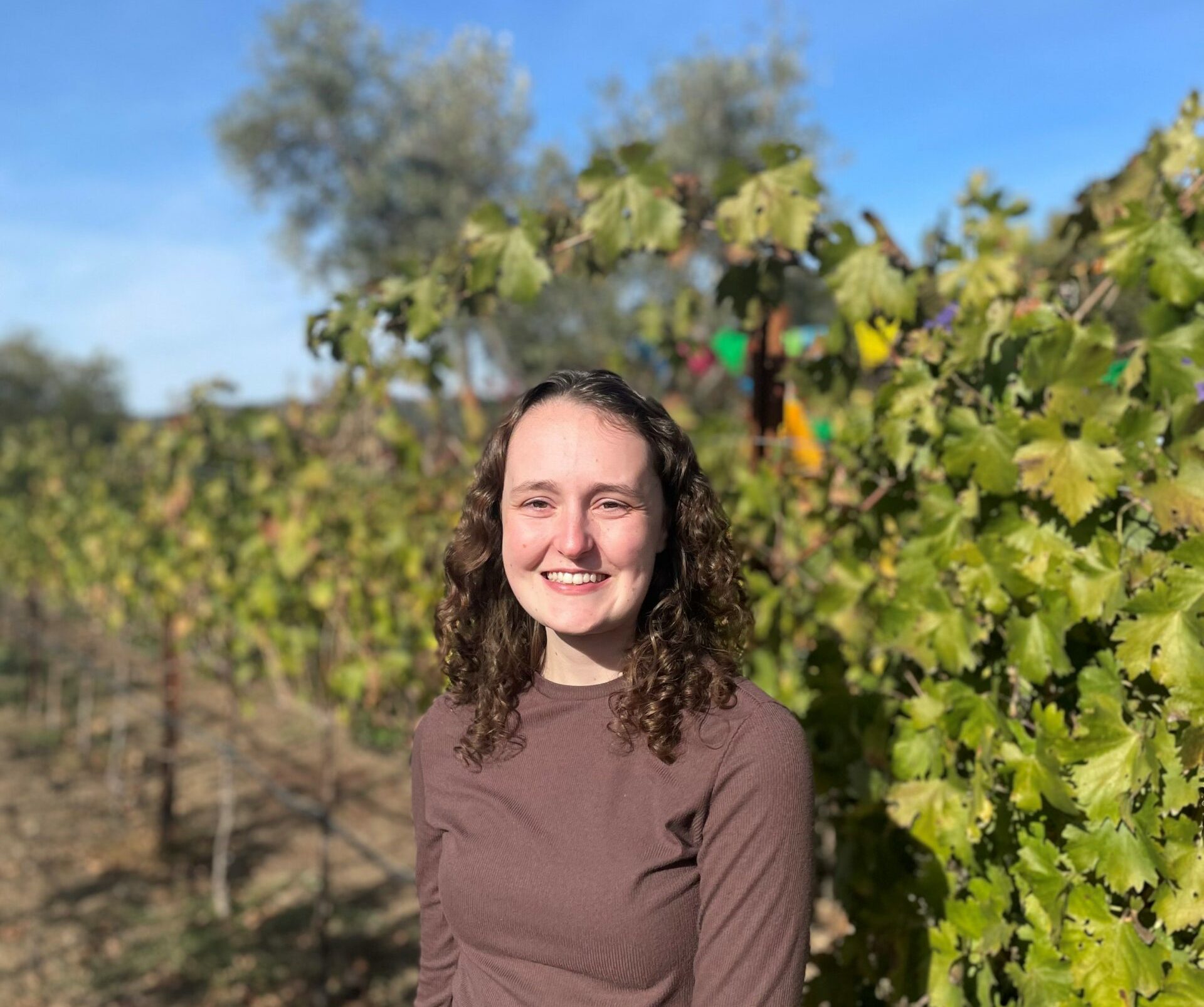 Kyla Botsian, wearing a brown shirt, stands in a vineyard