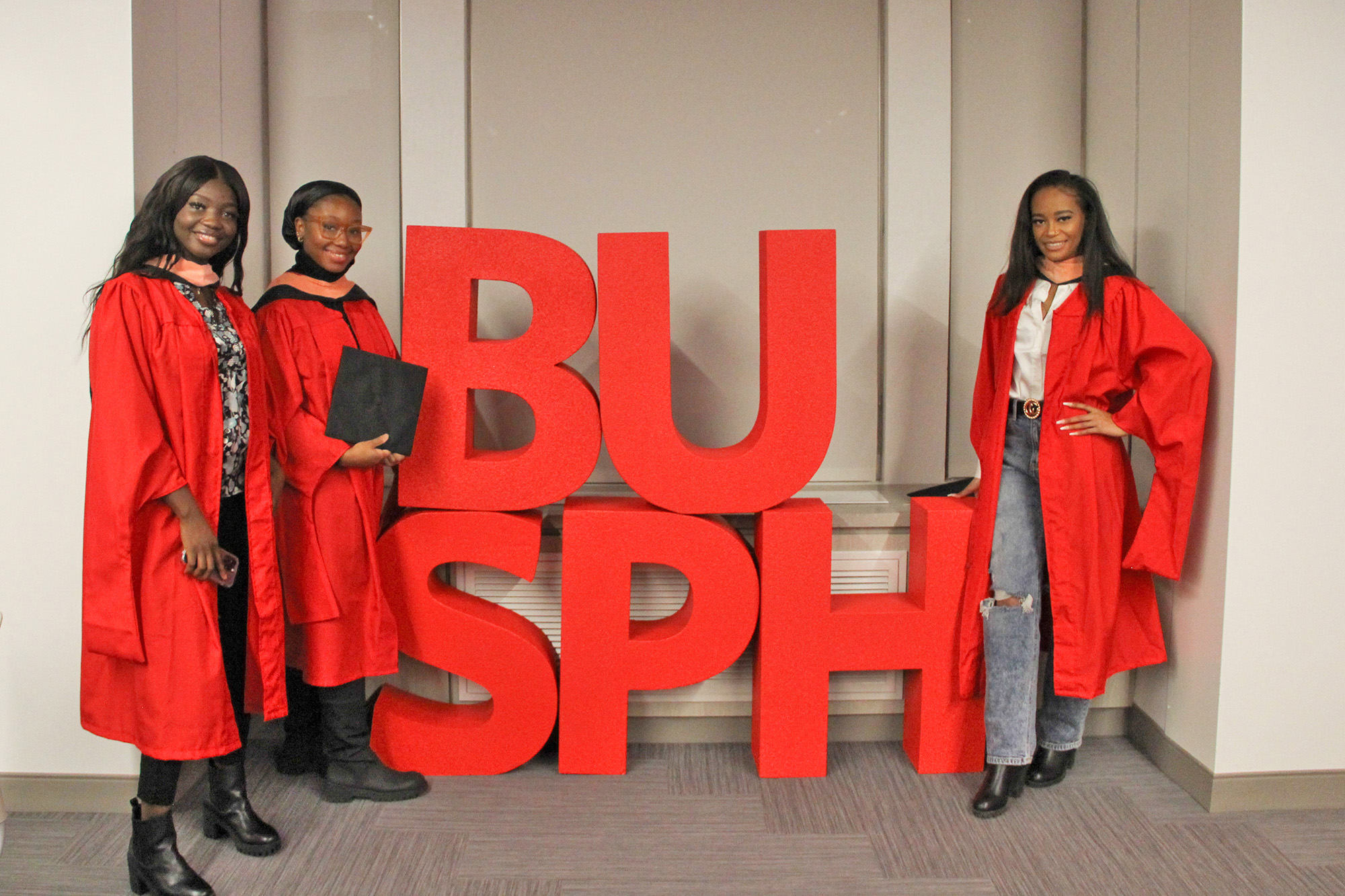 Three December 2022 grads stand with large red BUSPH letters