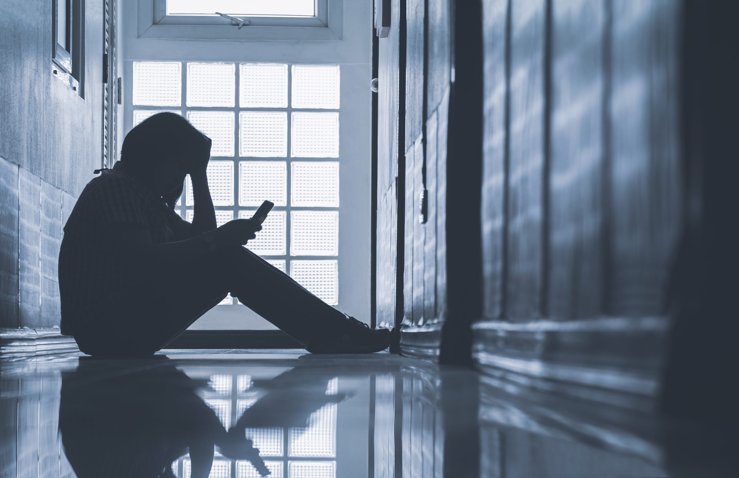 Woman sitting alone and looking smartphone with holding her head on corridor in front of room at apartment