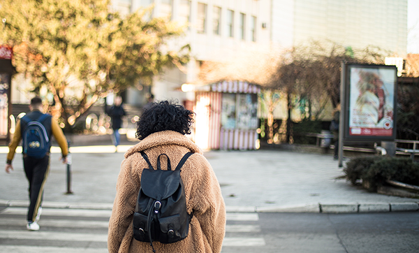 Woman wearing backpack walks in a city crosswalk