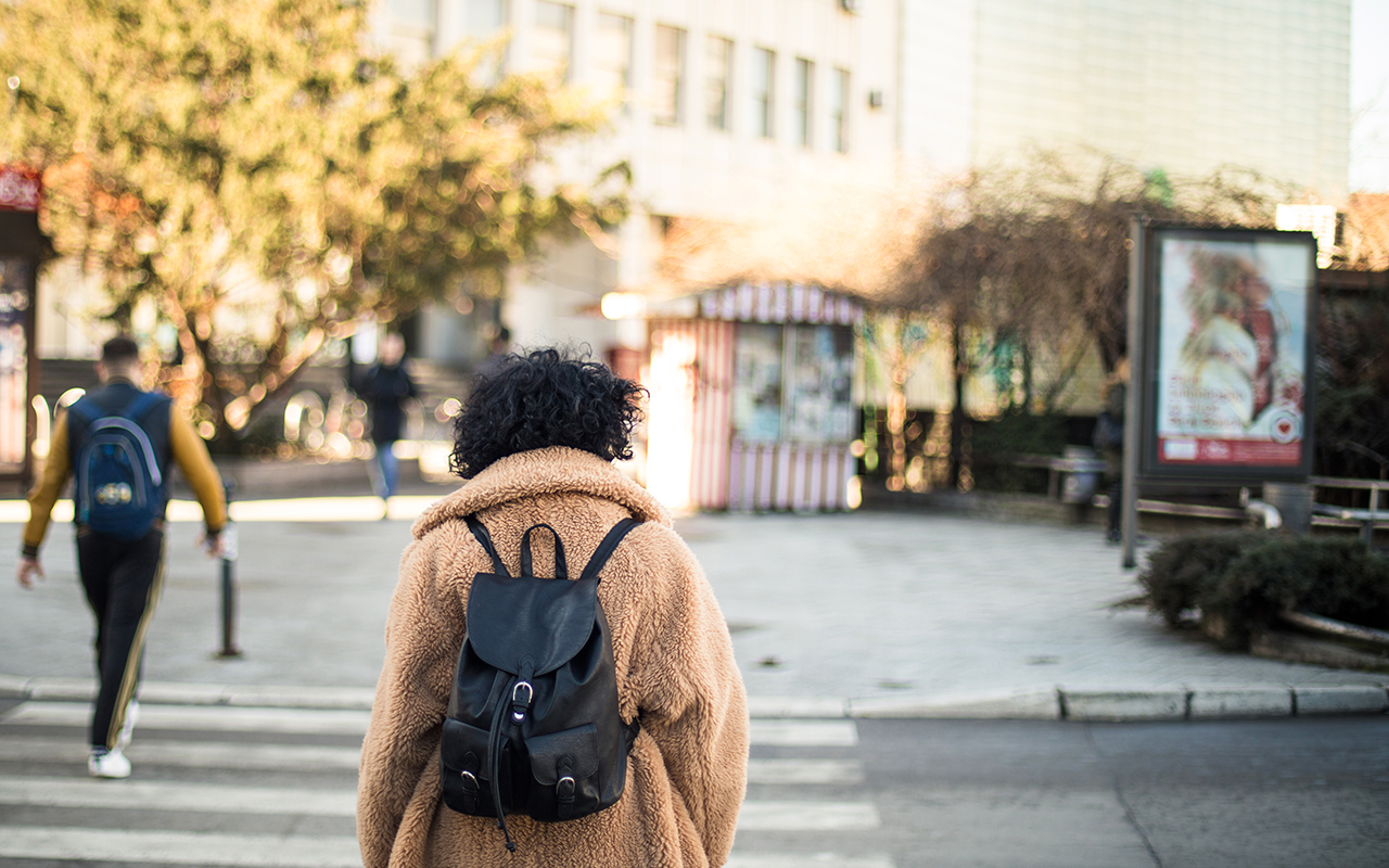 Woman wearing backpack walks in a city crosswalk