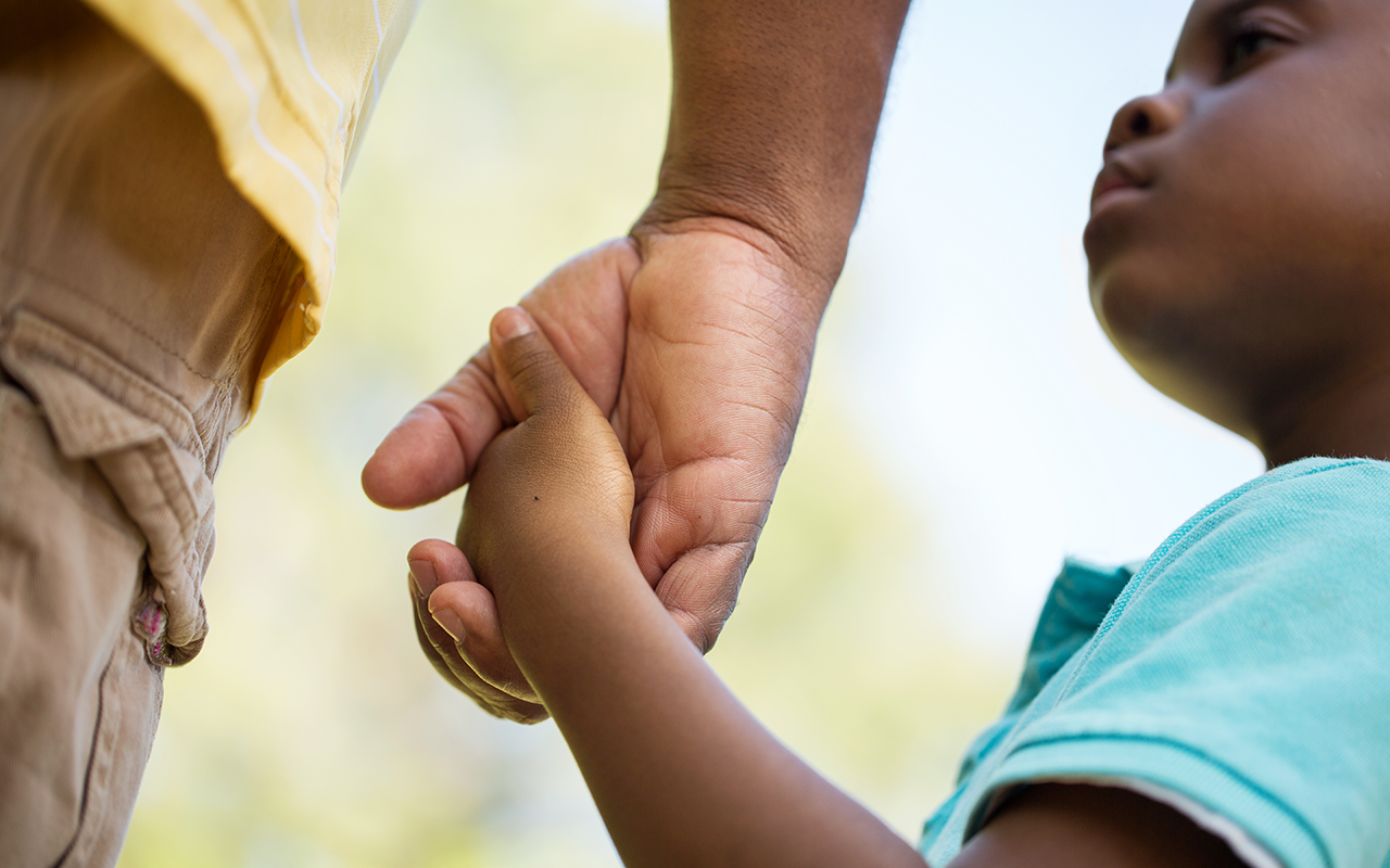 Small black boy holds hand of adult