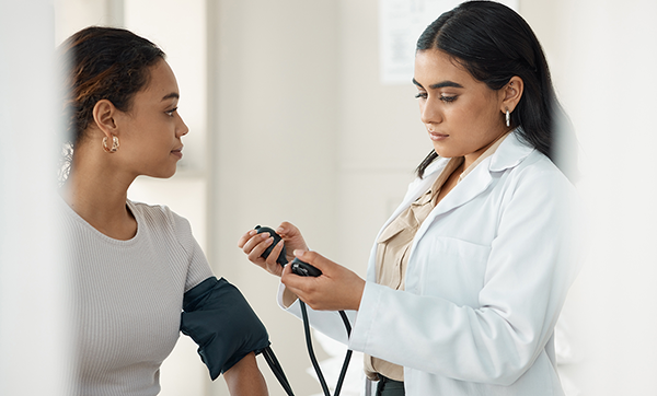 Shot of doctor standing and checking her patient's blood pressure during a consultation in the clinic