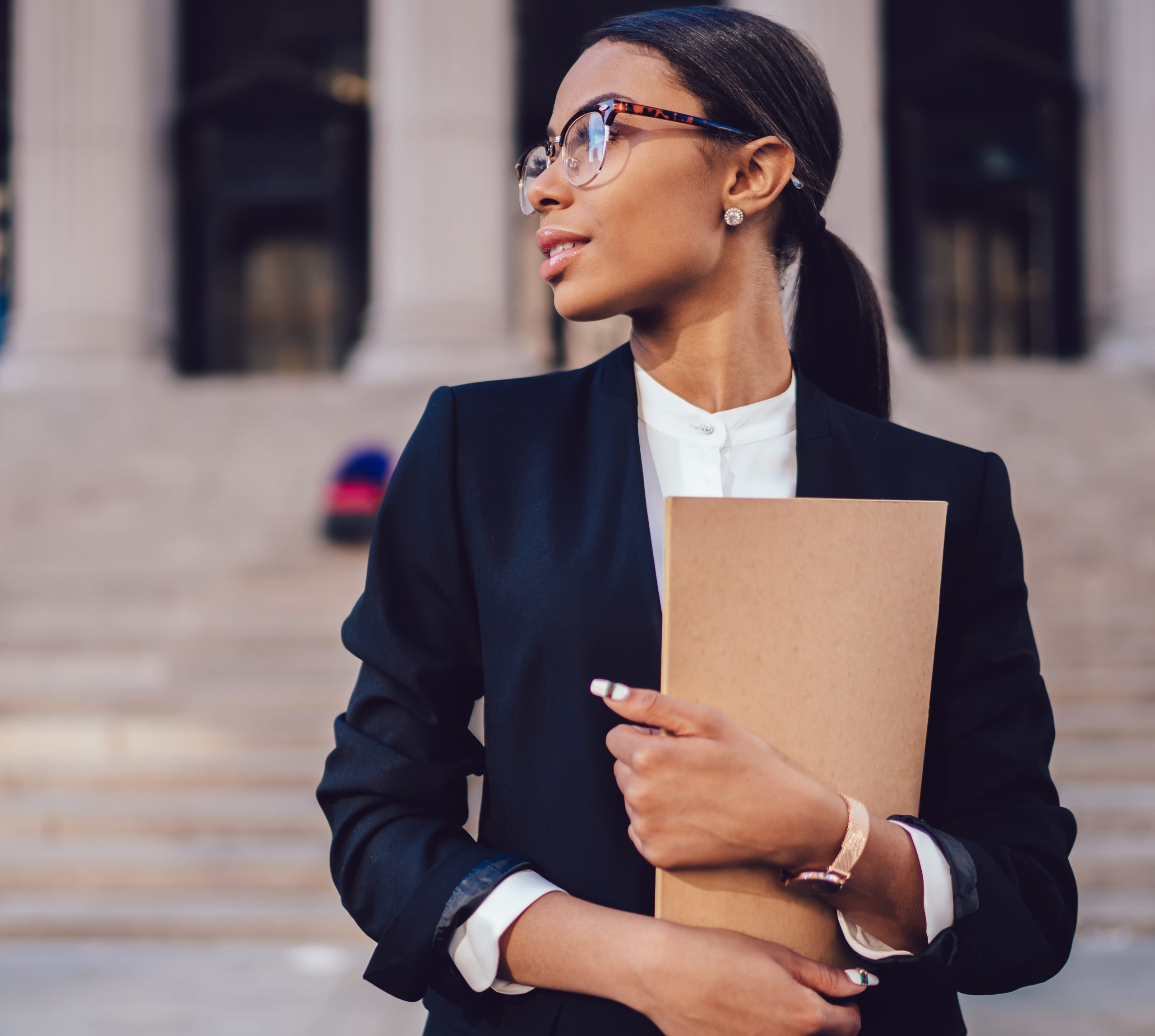 Female lawyer in stylish formal suit holding folder, looking away standing against courthouse