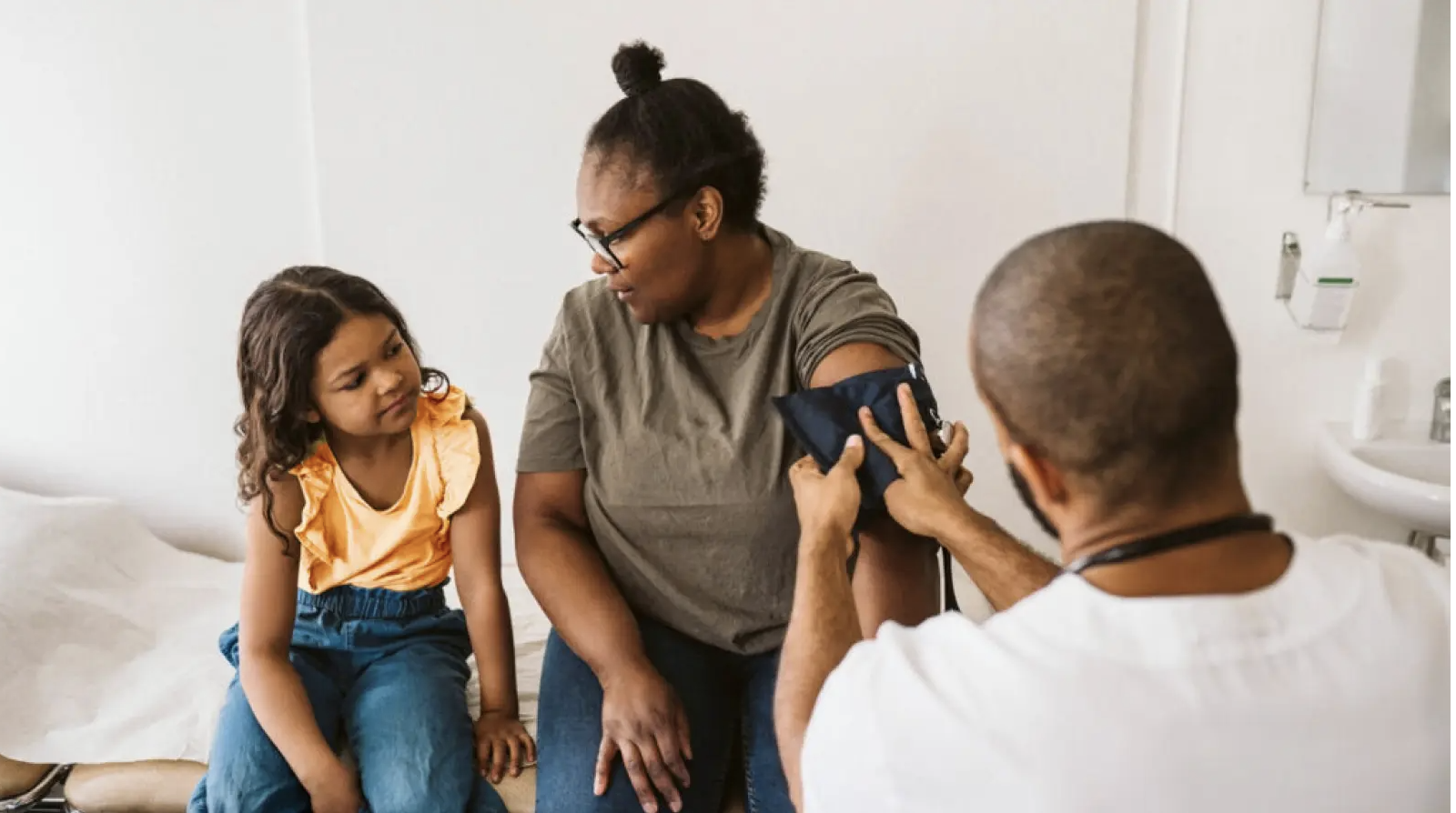 Nurse places blood pressure cuff on mother as her daughter watches