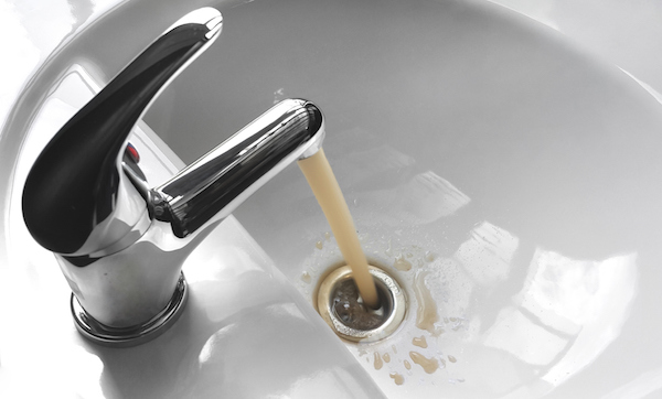 Water tap faucet with flowing contaminated muddy and dirty water in a white bathroom sink.