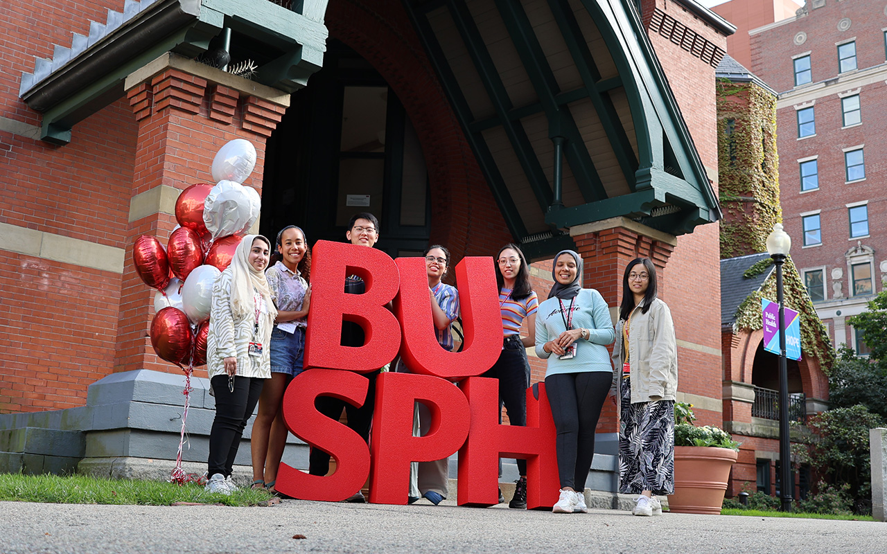 New students stand with large BUSPH letters in front of the Talbot building