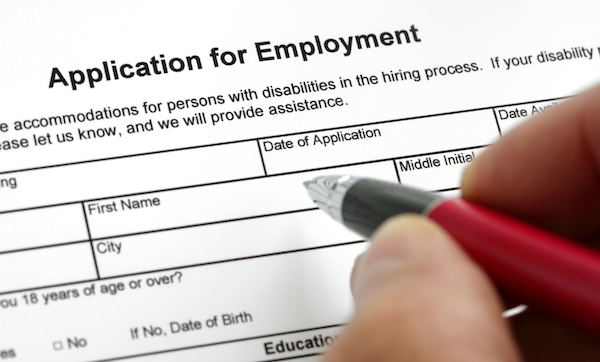 A hand with a pen filling out an application for employment