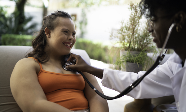 Doctor puts stethoscope to the chest of a woman with Down syndrome