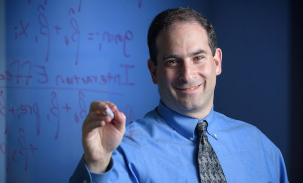 Headshot of alumnus Michael Posner holding a dry erase marker to a transparent board with statistical equations superimposed over his left shoulder