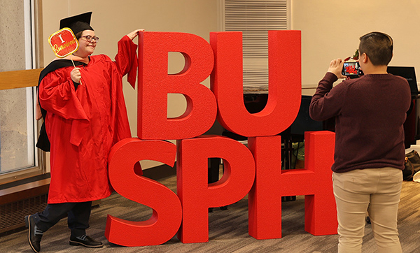 Recent grad celebrating at December ceremony beside BUSPH letters.