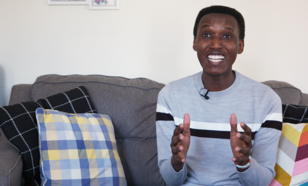 Alex Gitungano, sits on a couch, smiling and gesturing with his hands mid-conversation