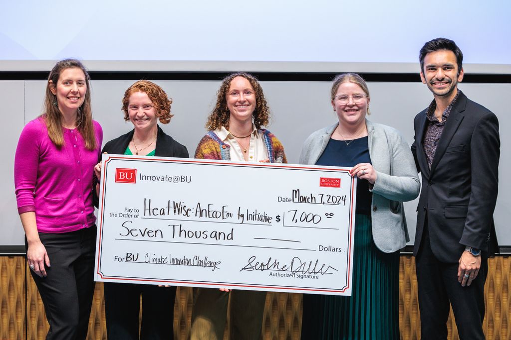 Megan Ryder stands holding a big large check beside four judges. The check reads: BU Innovate@BU. Date March 7, 2024. Pay to the Order of: Heatwise: An EcoEquity Initiative $7000.00 For: BU Climate Innovation Challenge."