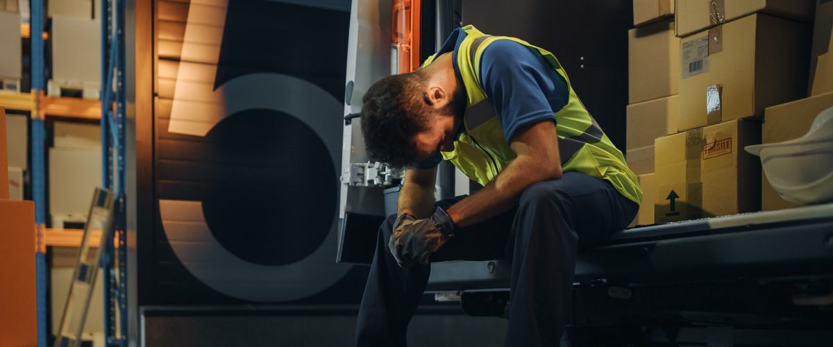 Male Worker Wearing Safety Vest Loads Cardboard Boxes into Delivery Truck, Rests. Dramatic Shot