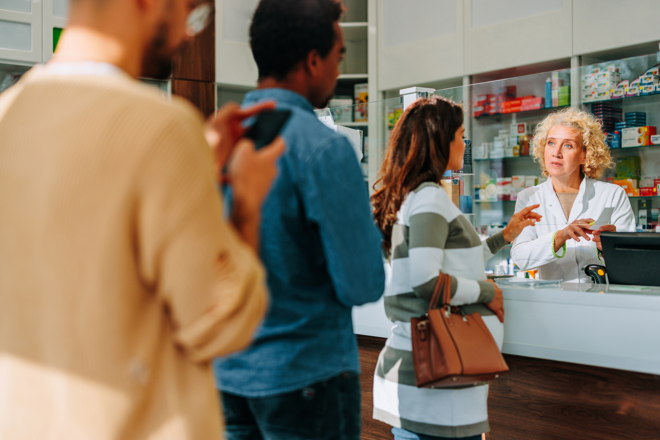 A number of people are in the pharmacy, standing in line behind a pregnant woman.