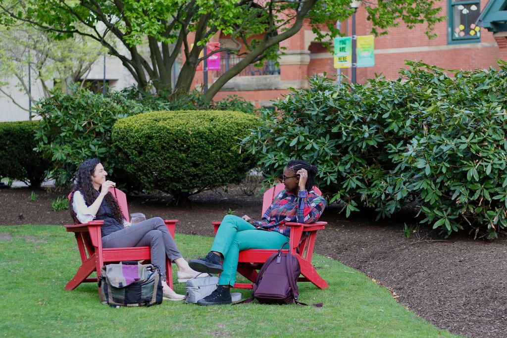 A pair of staff members having a bite to eat and a conversation in a pair of Adirondack chairs in front of the Talbot Building