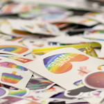 A rainbow, heart-shaped sticker that reads "Love Wins" sits atop a pile of Pride-related stickers.