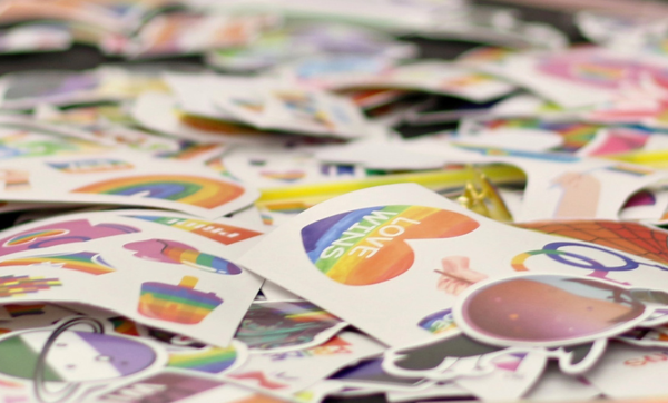 A rainbow, heart-shaped sticker that reads "Love Wins" sits atop a pile of Pride-related stickers.