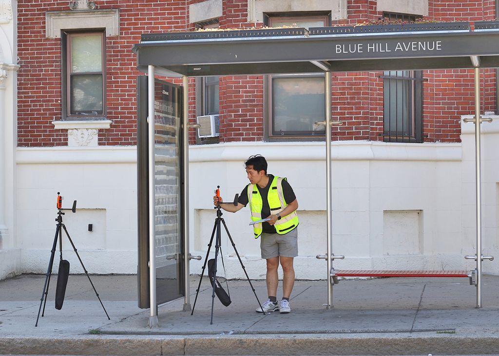 Jonathan Lee, a PhD student, checks a temperature sensor set up under the shade of the Blue Hill Avenue bus shelter in Dorchester. A second sensor sits outside the bus shelter to the left.