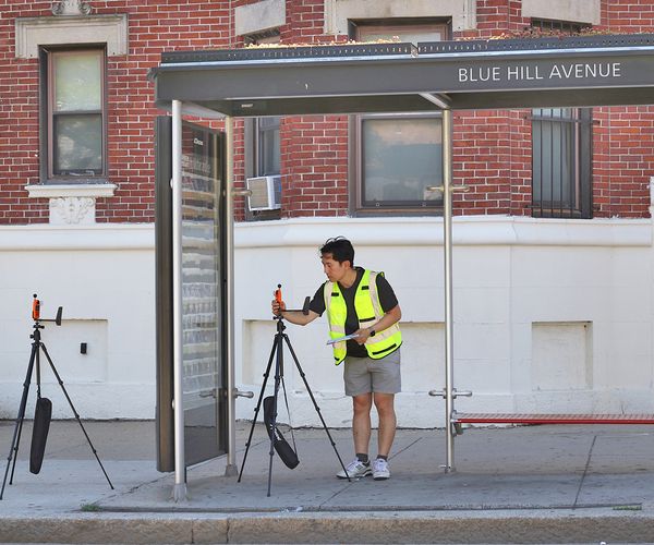 Jonathan Lee, a PhD student, checks a temperature sensor set up under the shade of the Blue Hill Avenue bus shelter in Dorchester. A second sensor sits outside the bus shelter to the left.