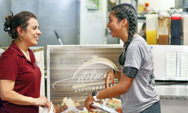 Victoria A. Lopez (right), an MPH student, explains how the wearable temperature sensor on her left arm works to a potential study participant at a restaurant in Chelsea.