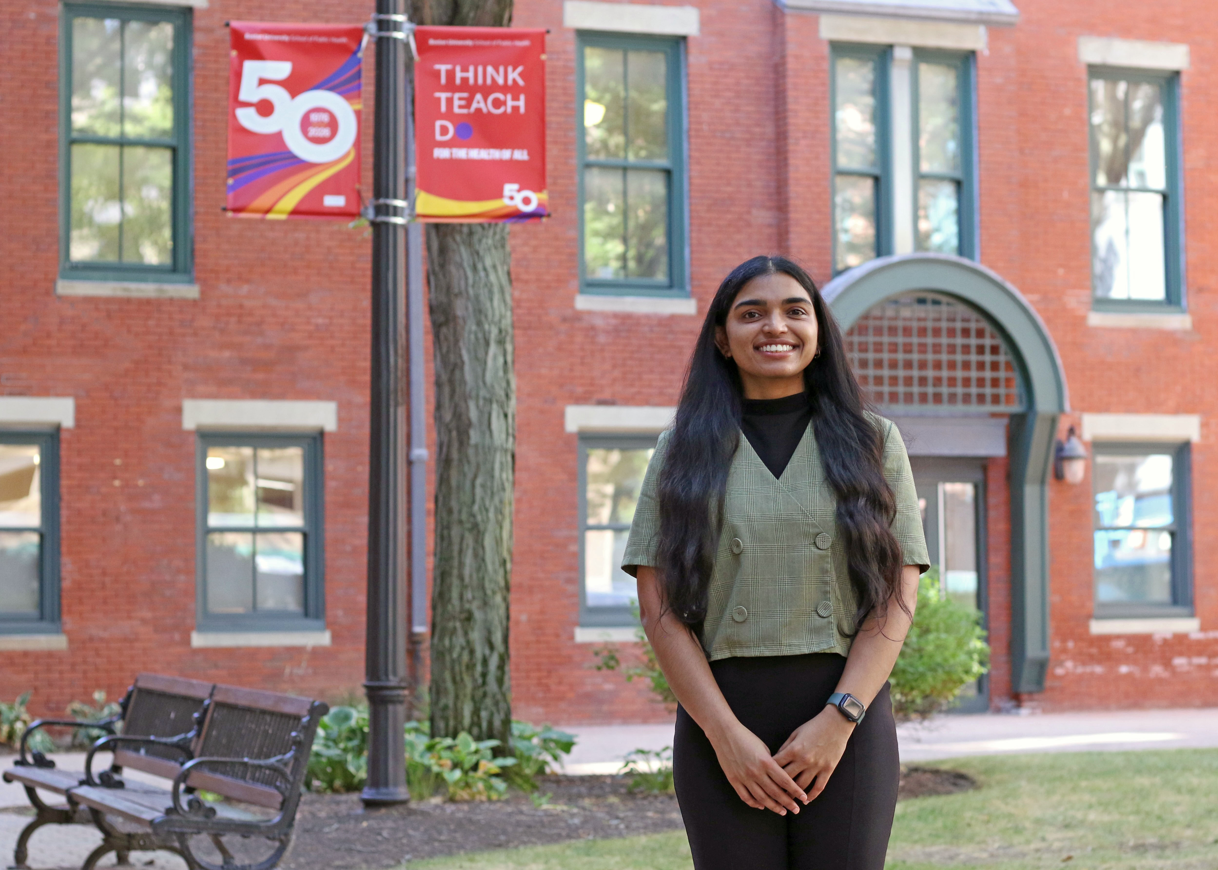 Anushka Reddy Marri stands before the Talbot Building in front of a banner celebrating the School's 50th anniversary.