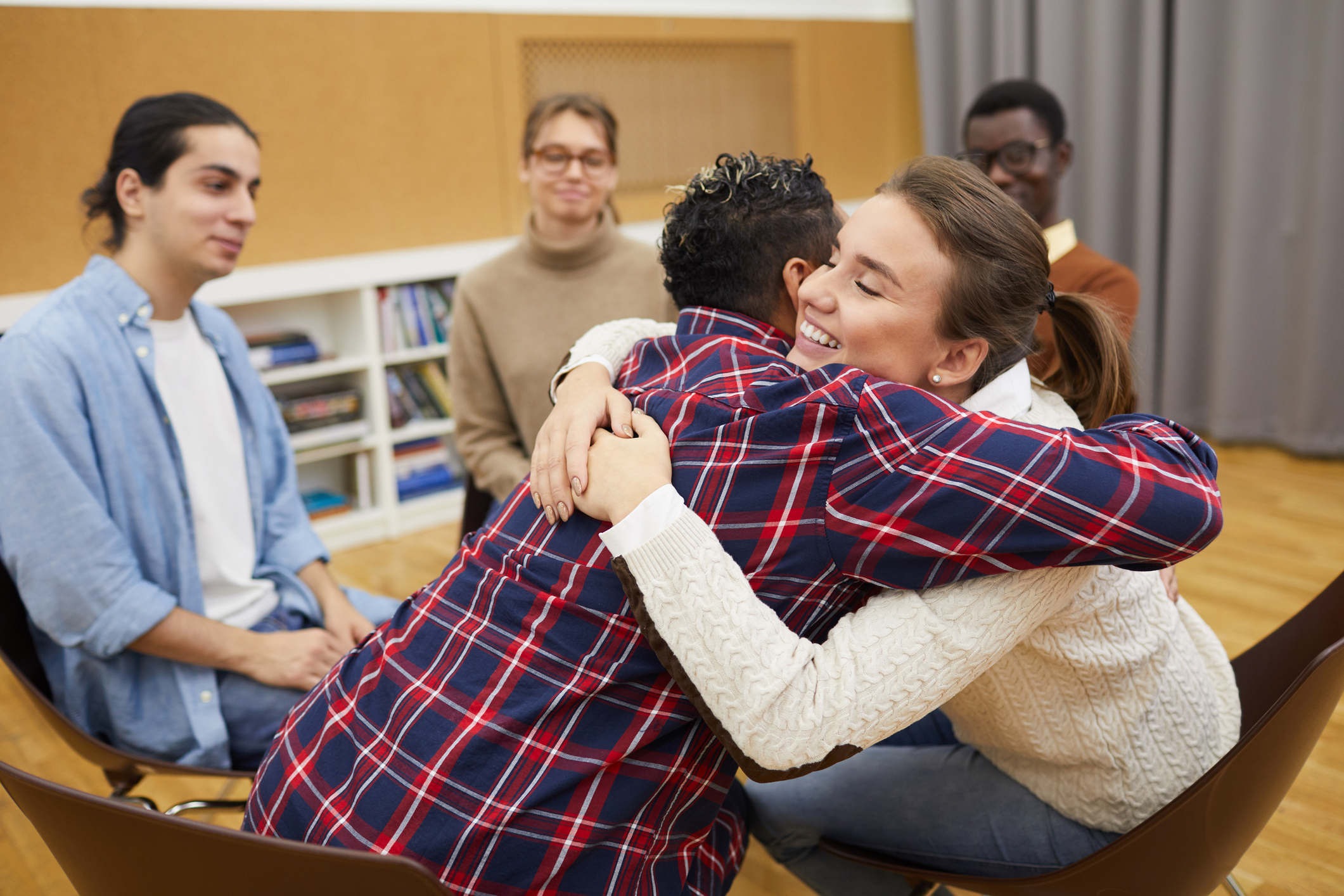 Portrait of two young women hugging in support group meeting, both smiling happily, copy space