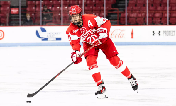 Julia Shaunessy, wearing the #20 BU jersey, skates across the ice with a puck at the end of her hockey stick