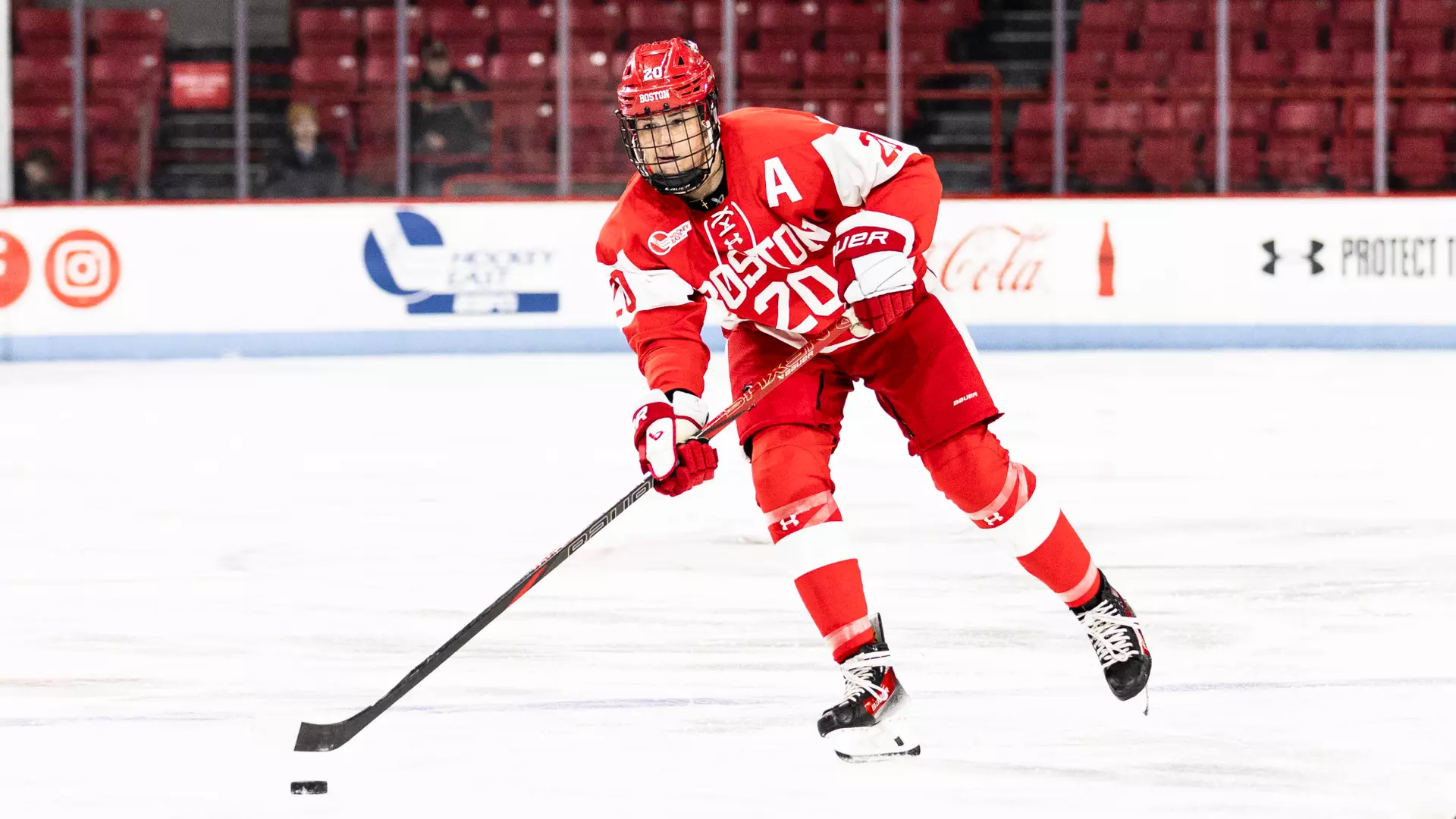Julia Shaunessy, wearing the #20 BU jersey, skates across the ice with a puck at the end of her hockey stick