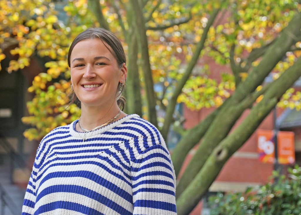 Julia Shaunessy smiles in a white-and-blue striped sweater in front of the Talbot Building in fall.